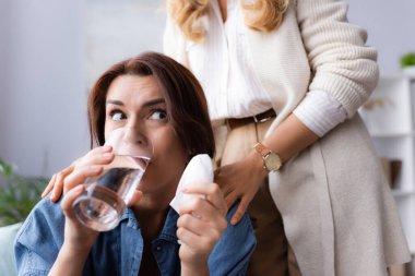 Terapist hastayı sakinleştirirken esmer kadın su içiyor.