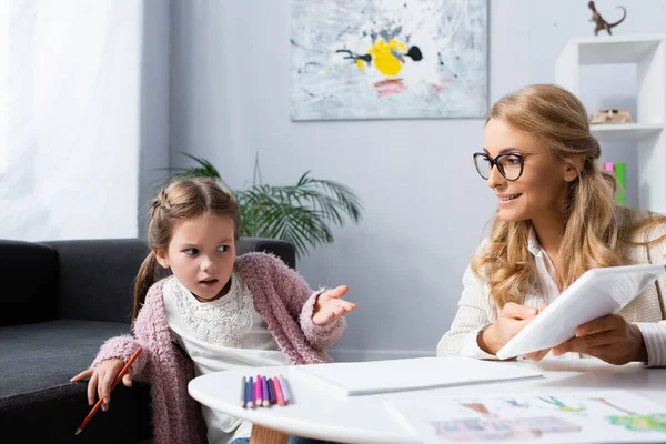 Menina Confusa Com Lápis Mostrando Tablet Digital Enquanto Visita Psicólogo — Fotografia de Stock