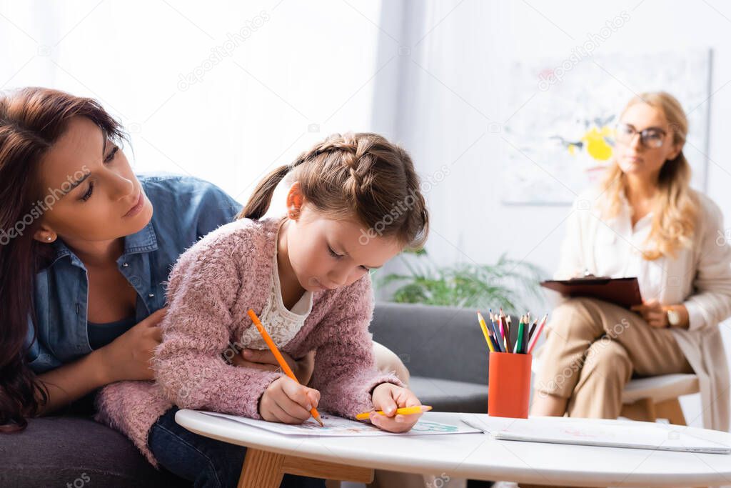 little girl patient drawing picture while visiting psychologist with mother