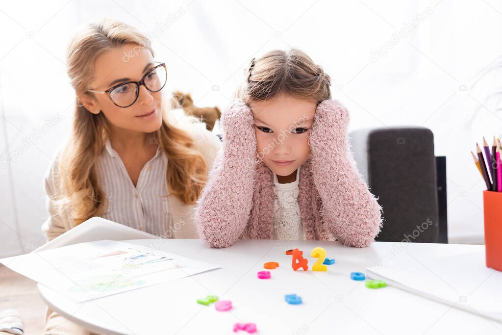 girl patient resting head on hands while calculating with figures near psychologist