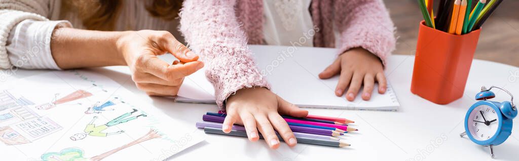 cropped view of little girl drawing pictures with colorful pencils while visiting psychologist, banner