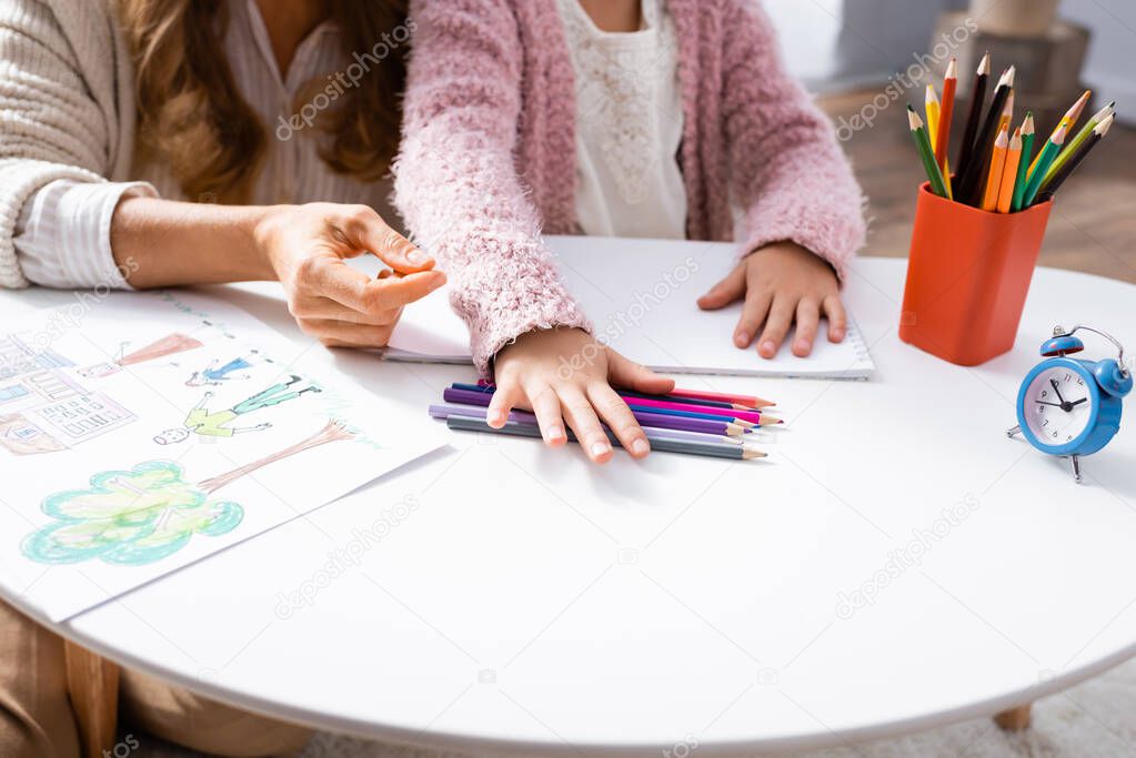 cropped view of little girl drawing pictures with colorful pencils while visiting psychologist