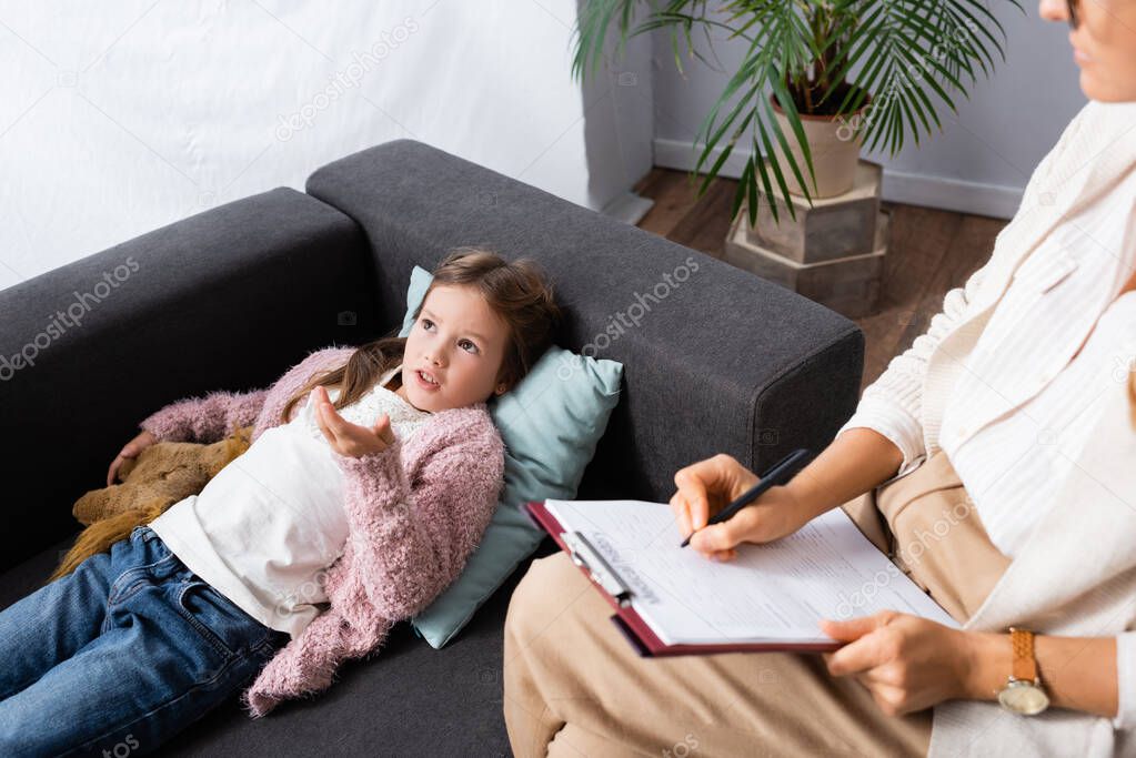 little girl lying on sofa with toy while telling problem to psychologist