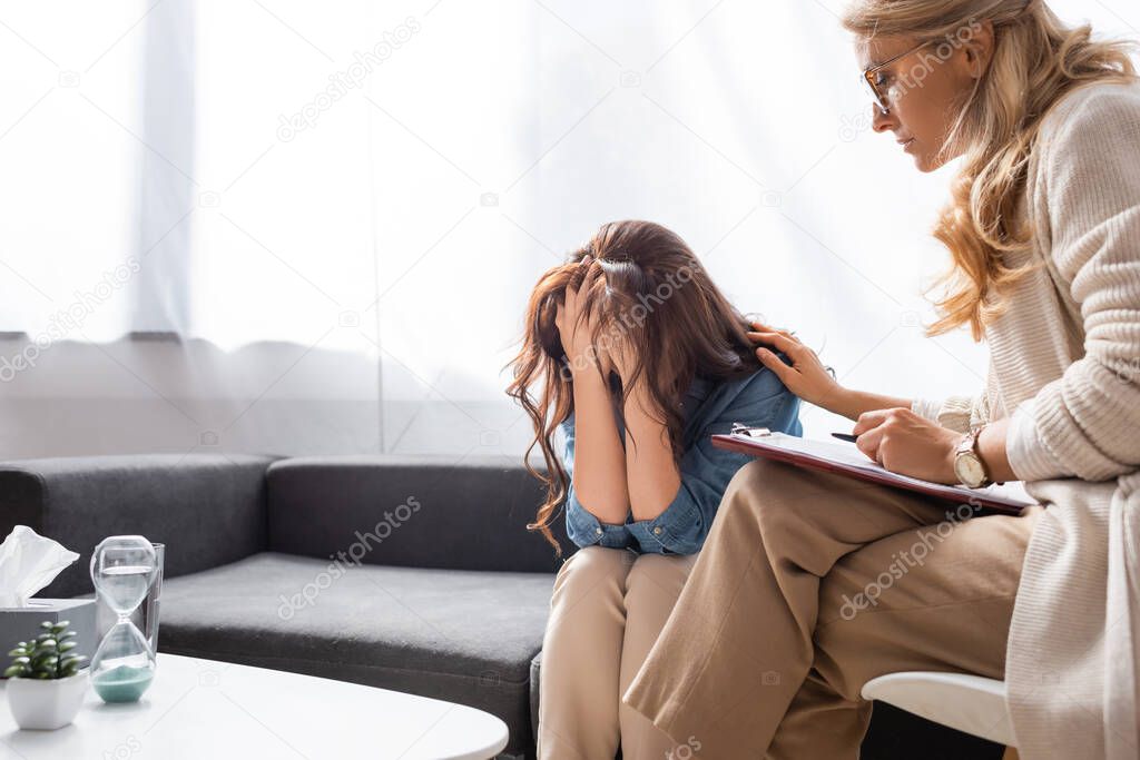 brunette woman covering face while therapist calming patient down 