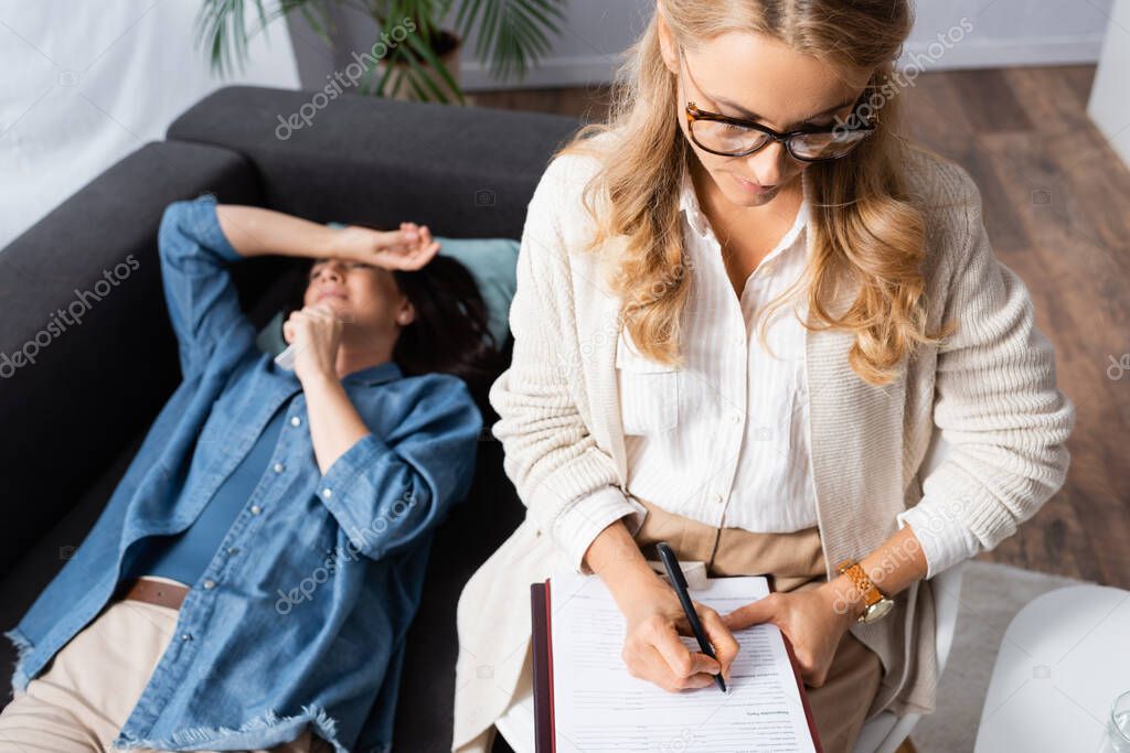 blonde woman therapist making notes in medical history of patient