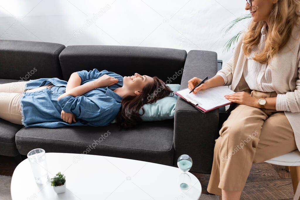 happy brunette woman lying on sofa while visiting therapist