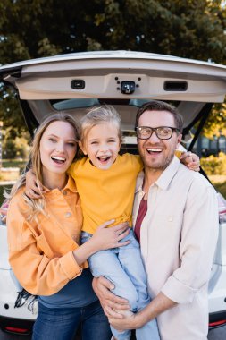 Neşeli kız araba gezisi sırasında anne ve babasına sarılıyor. 