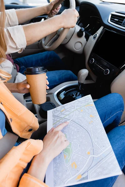 Cropped view of woman with coffee to go pointing at map while husband driving car