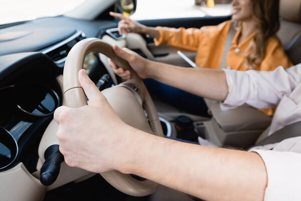 Cropped view of man driving car near wife pointing with finger on blurred background 