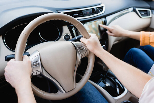 Cropped view of man driving auto while wife using audio system on blurred background 
