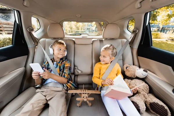 Gyerekek Okostelefonnal Könyv Mosolygós Egymás Közelében Játékok Autóban — Stock Fotó