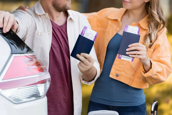 持护照和机票的妇女在室外汽车附近拥抱丈夫的照片 — 图库照片