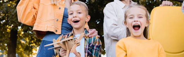 スーツケース屋外 バナー付きの親の近くに立っておもちゃの飛行機を持つ陽気な子供たち — ストック写真