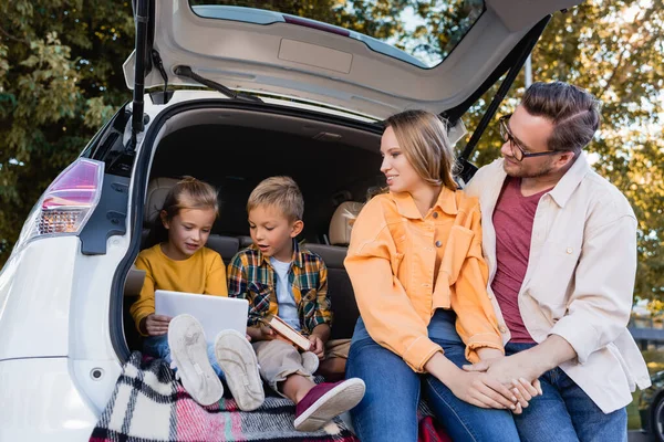 Smiling Parents Holding Hands Looking Kids Book Digital Tablet Trunk — Stock Photo, Image