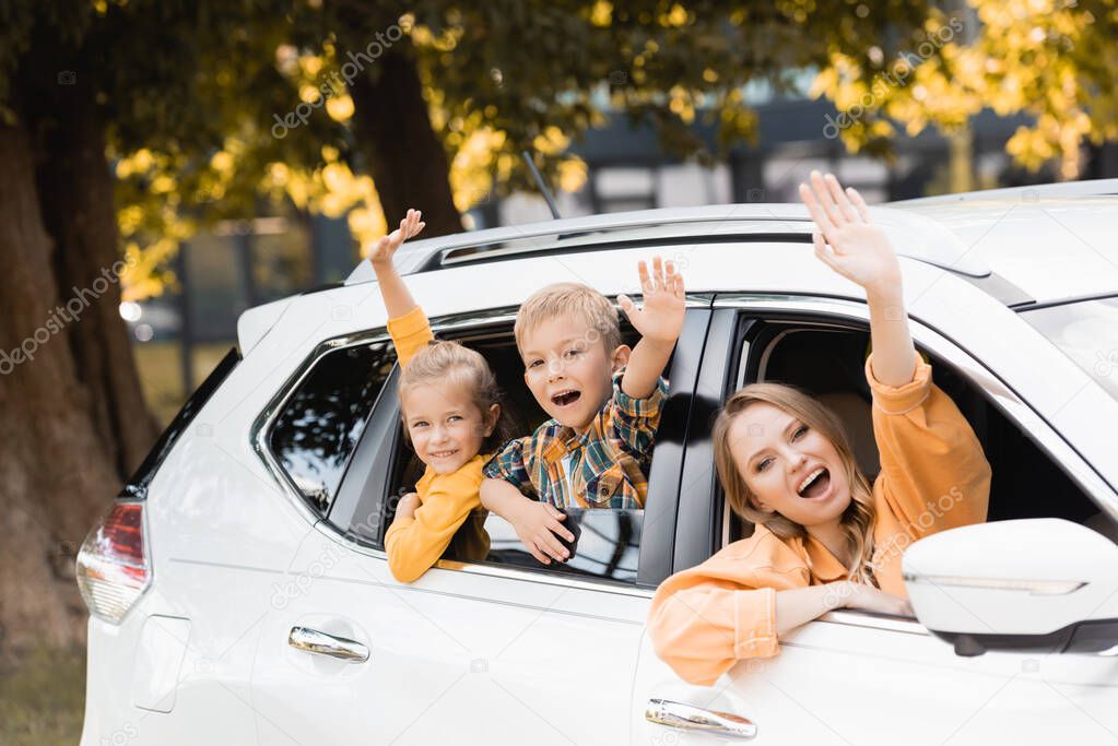 Smiling children waving hands near mother during travel in car 