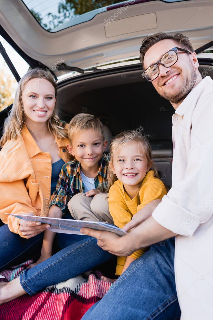 Smiling family holding map while looking at camera in trunk of car 