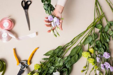 Çiçekçinin elinde makas, secateurs ve dekoratif kurdeleyle buket yaparken elinde çiçek tutuşu.