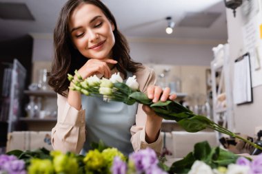 Çiçekçide, bulanık önplanda çiçeklerin yanında Eustoma 'yı tutan mutlu çiçekçi.
