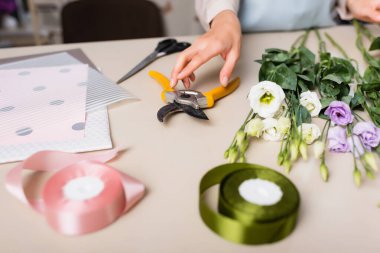 Çiçekçinin, Eustoma çiçeklerinin yanında mezecileri alıp ön planda bulanık dekoratif kurdele takması.