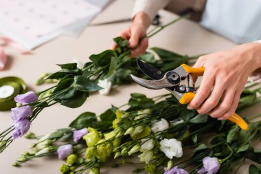 Önplanda bulanık buket yaparken elinde çiçekçiler ve Eustoma çiçekleri olan çiçekçi manzarası.