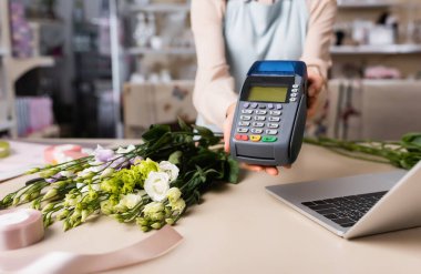 Laptop, Eustoma çiçekleri ve bulanık arkaplanda dekoratif kurdele bulunan çiçekçi ödeme terminalinin kırpılmış görüntüsü