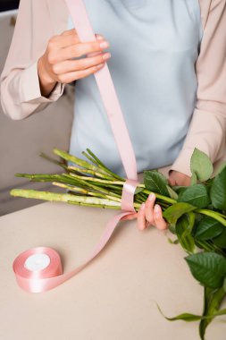 Cropped view of female florist with decorative ribbon tying stalks of bouquet on desk clipart