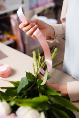 Close up view of florist hand holding decorative ribbon, while tying stalks of bouquet in flower shop on blurred background clipart