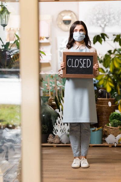 full length view of florist in protective mask holding board with closed lettering on blurred foreground