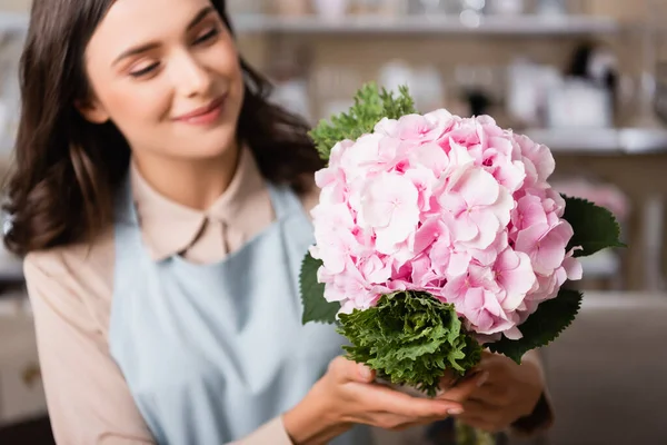 在模糊的背景下 微笑着的女花匠看着花店里盛开的水仙花 — 图库照片