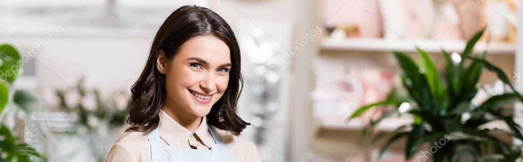 happy florist looking at camera in flower shop on blurred background, banner