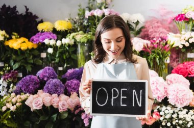 Excited florist looking at chalkboard with open lettering near range of flowers on background clipart
