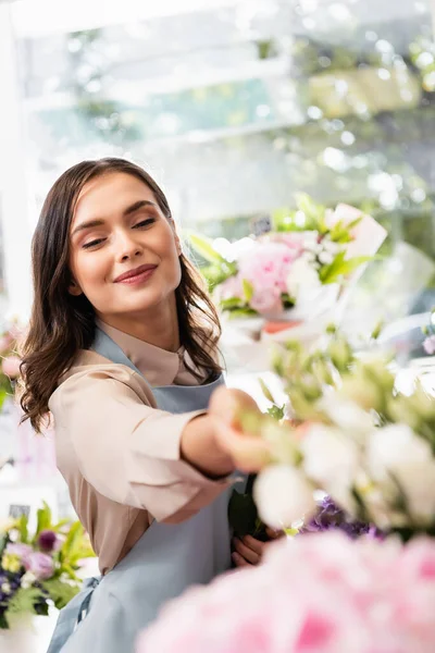 Sorrindo Florista Feminina Com Mão Estendida Olhando Para Flores Borradas — Fotografia de Stock