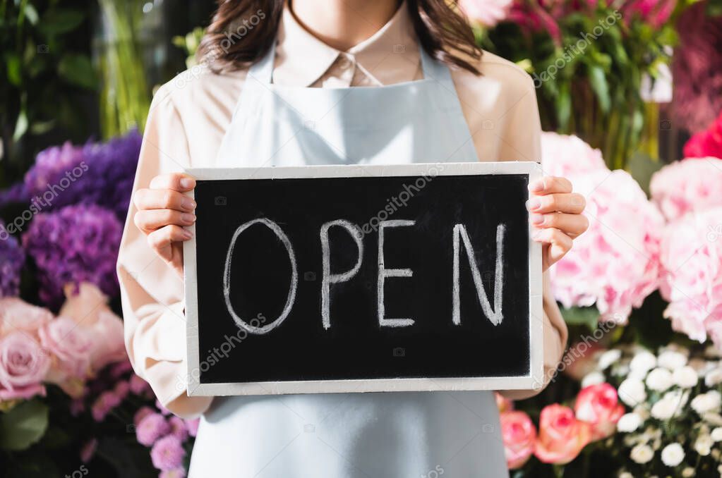 Cropped view of florist holding chalkboard with open lettering with blurred range of flowers on background