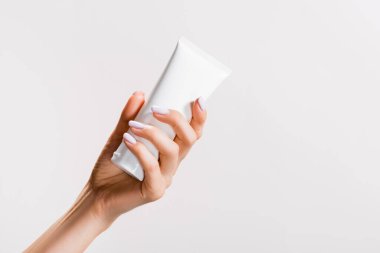 cropped view of woman holding tube of hand cream isolated on grey clipart