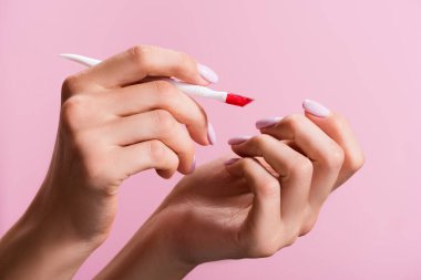 cropped view of woman using cuticle pusher isolated on pink clipart