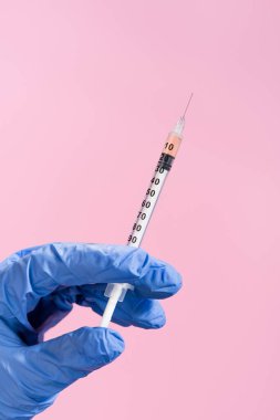 Kırpılmış, lateks eldivenli, pembe üzerine izole edilmiş bir şırınga.