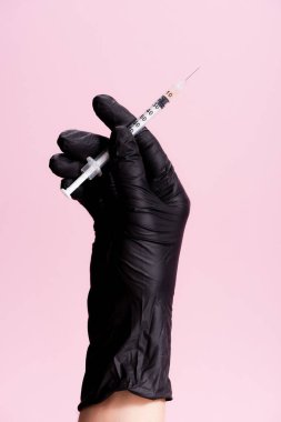 Kırpılmış siyah lateks eldivenli el görüntüsü ve pembe üzerine izole edilmiş şırınga.