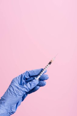 Kırpılmış mavi lateks eldivenli el görüntüsü ve pembe üzerine izole edilmiş şırınga.