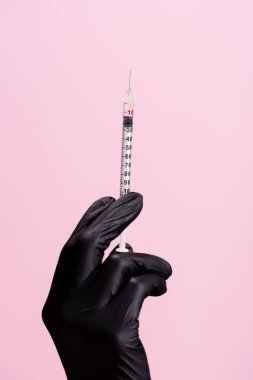 Kırpılmış siyah lateks eldivenli el görüntüsü ve pembe üzerine izole edilmiş şırınga.