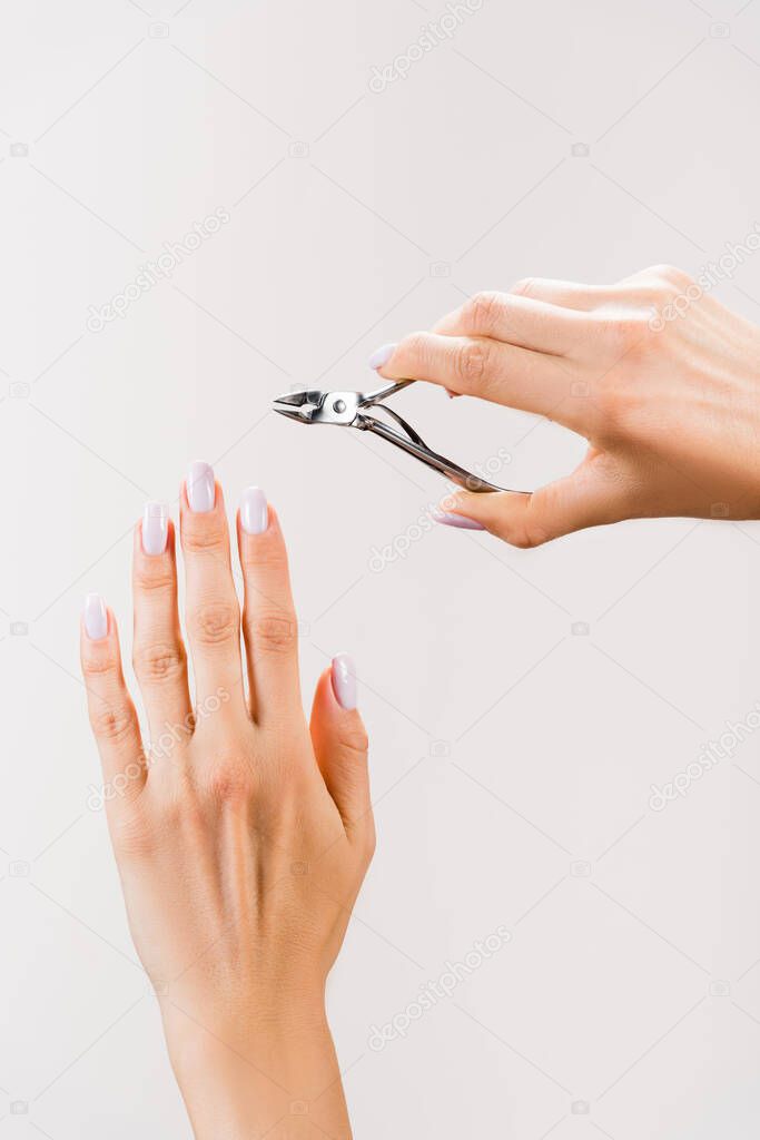 cropped view of woman holding cuticle nipper isolated on grey