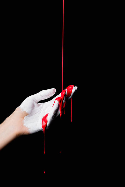 partial view of white painted hand with red dripping paint isolated on black