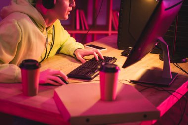 Akıllı telefonun yanında bilgisayar kullanan oyuncu görüntüsü, bulanık ön planda pizza ve kahve almak. 