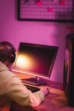 Bulanık arkaplanda kulaklıktaki oyuncunun yanında boş ekran olan bilgisayar monitörü 