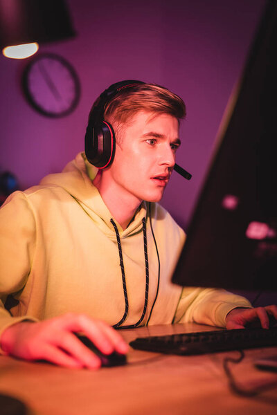 Focused man in headset playing video game on computer on blurred foreground 