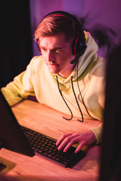 Young man in headset using computer keyboard during video game 