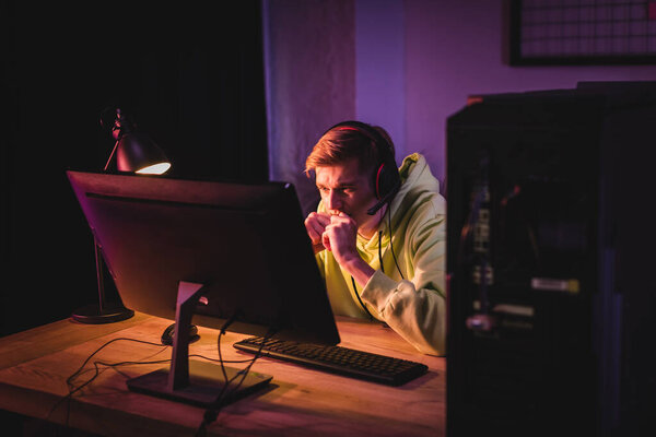 Tensed gamer in headset looking at computer monitor during video game at home 