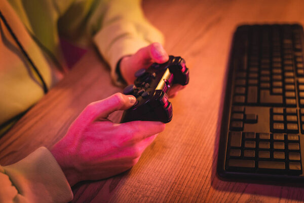 KYIV, UKRAINE - AUGUST 21, 2020: Cropped view of gamer using joystick near computer keyboard on blurred background 