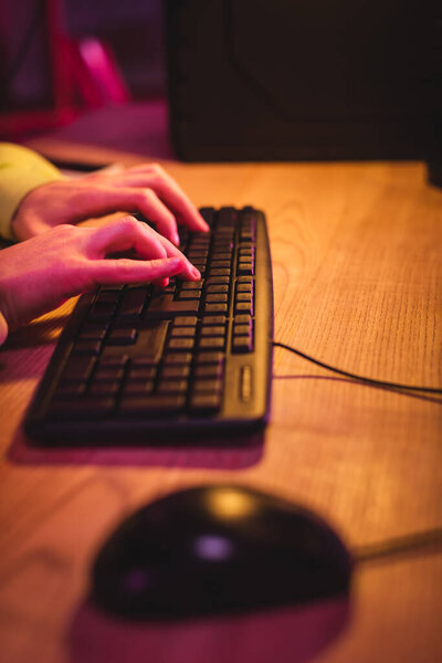 Cropped view of gamer using computer keyboard near mouse on blurred foreground on table 