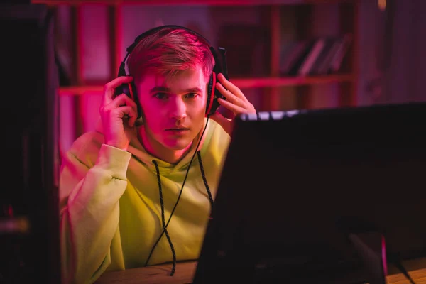 Young Gamer Holding Headphones Looking Camera Computer Monitor Blurred Foreground — Stock Photo, Image