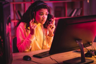KYIV, UKRAINE - 21 AĞUSTOS 2020: Heyecanlı Afro-Amerikan oyuncu kulaklıkla evde bilgisayar, joystick ve akıllı telefon başında oturuyor 
